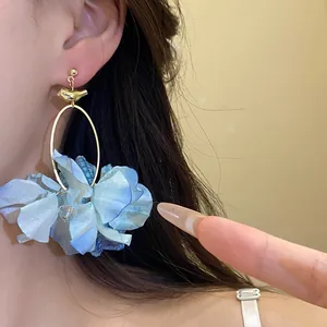 Dettaglio di orecchini pendenti con fiori di stoffa blu, uccellino dorato e cerchio.
