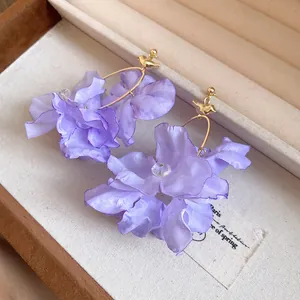 Primo piano di orecchini a fiore in tessuto lavanda con perni a forma di uccello dorati.
