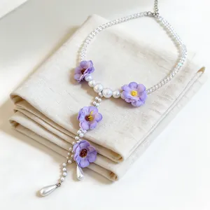 Dettaglio di una collana a Y con fiori in tessuto viola e perle bianche eleganti