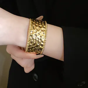 Detailansicht eines eleganten goldenen Metallarmreifs mit gehämmerter Textur und Perlenrand