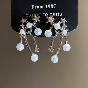 Dettaglio di orecchini pendenti con stelle e perle con ago in argento e cristalli.