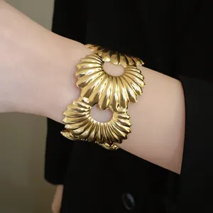 Detailaufnahme einer breiten goldenen Manschette mit Faltenstruktur und runden Ausschnitten