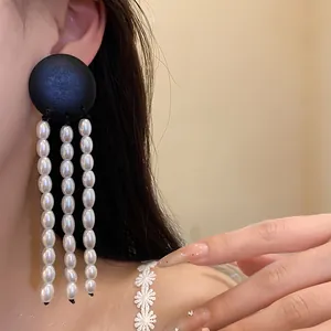Detailed view of vintage black wood disc and white pearl tassel earrings on model