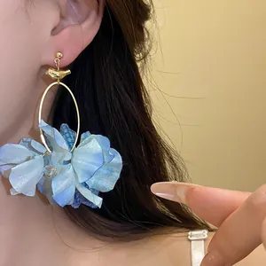 Dettaglio di orecchino a fiore in tessuto blu con cerchio dorato indossato da modella