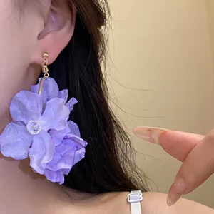 Dettaglio di grandi orecchini a fiori in tessuto viola che mostrano la trama dei petali