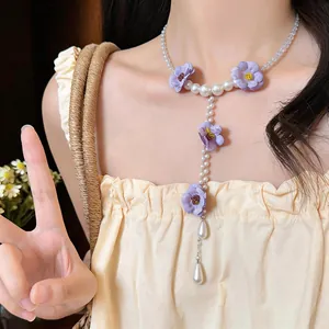 Vista macro dettagliata dei fiori in tessuto viola e nappe di perle su collana stile coreano