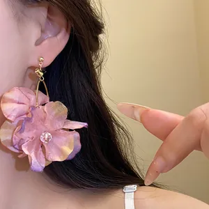 Dettaglio di grandi orecchini pendenti a fiore in tessuto rosa stile vacanza