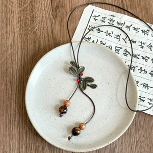 Close-up of a vintage bronze leaf pendant with bodhi beads displayed on a white ceramic plate