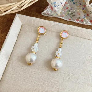 Close-up detail of French elegant pearl drop earrings with iridescent pink studs and gold finish