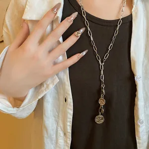 Detailed macro shot of a silver chain necklace featuring vintage coin pendants and tassels.