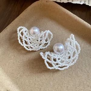 Detailed view of white beaded earrings with central pearl and silver needle
