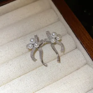 Close-up view of silver bow stud earrings featuring delicate pearls in a jewelry box.