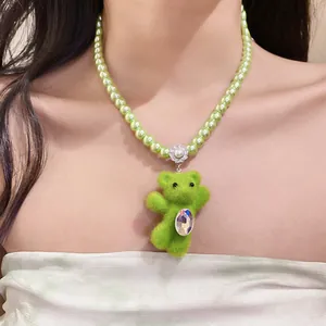 Detailed close-up of a green flocked bear pendant on a pearl necklace worn by a model
