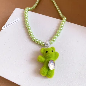 Detailed view of a green flocked teddy bear pendant on a light green pearl necklace