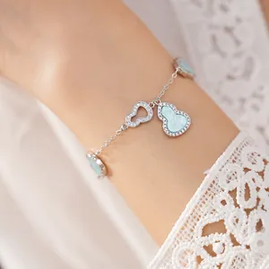 Macro view of a silver bracelet with light blue zircon-studded hollow gourd charms on wrist.