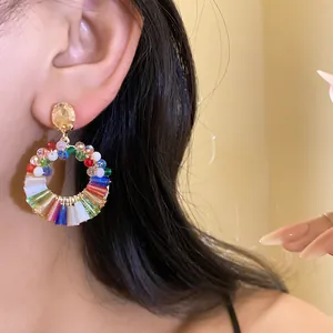 Close-up view of vibrant multi-colored crystal and bead circular hoop earrings worn on ear.
