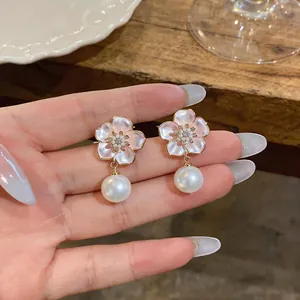 Close-up of pink cherry blossom enamel stud earrings with elegant pearl dangles