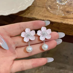 Detail shot of pink enamel cherry blossom earrings with elegant pearl drops held by hand.