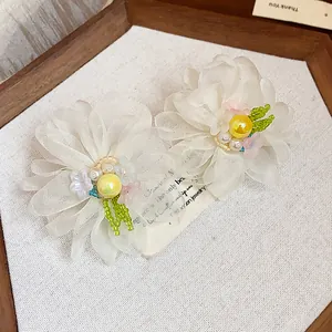 Close-up detail of elegant white chiffon flower stud earrings with yellow pearl accents.