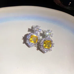 Close-up of elegant silver earrings with square yellow zircons and starburst effects
