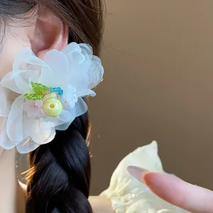 Close-up of white chiffon flower earrings with colorful bead accents worn on ear.