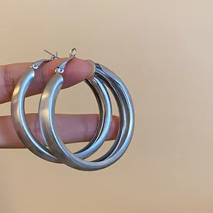 A detailed macro view of minimalist large brushed silver hoop earrings with a matte texture