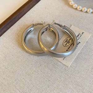 Close-up of minimalist brushed silver-tone hoop earrings on a neutral fabric background