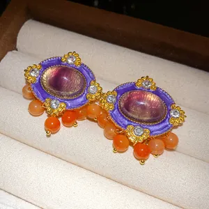 Macro detail of luxury vintage palace style earrings with purple resin and orange beads.