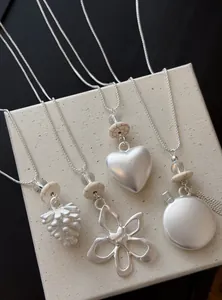 Vue détaillée de colliers argentés avec pendentifs en forme de cœur, fleur et pomme de pin.