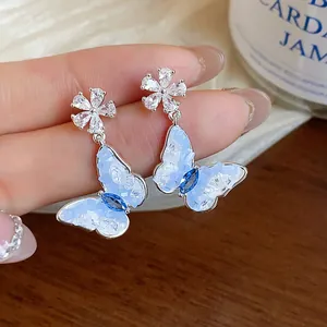 Close-up of sparkling zircon butterfly and flower stud earrings with blue crystalline wings