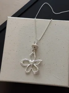 Détail d'un pendentif en forme de fleur argentée avec un cœur gravé et des perles décoratives