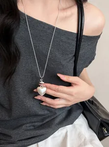 Gros plan d'un collier pendentif cœur argenté style coréen sur un haut gris.