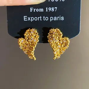 Dettaglio di orecchini a cuore placcati in oro 18k con zirconi e finitura testurizzata.