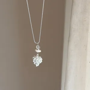 Gros plan d'un collier de perles argentées avec un pendentif blanc en forme de pomme.