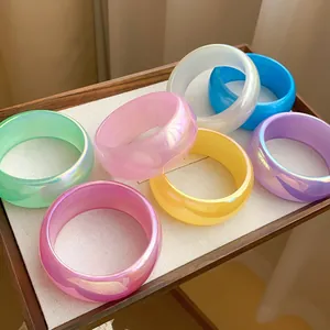 Varios brazaletes de resina iridiscente en colores vibrantes en una bandeja de madera