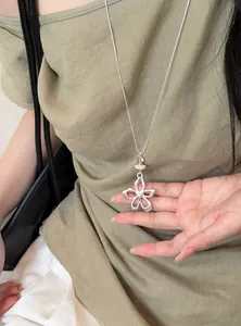 Gros plan d'un collier avec pendentif fleur argentée et cœur sur fond lin vert naturel