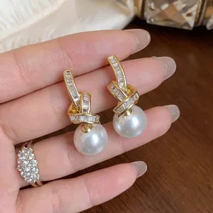 Elegant gold-tone knotted earrings featuring sparkling zircon accents and lustrous white pearls