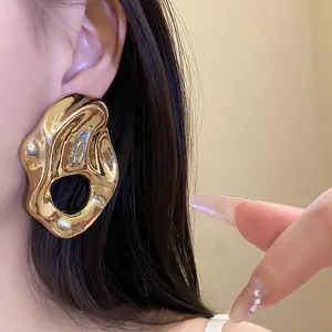 Detalle de pendientes dorados grandes irregulares con diseño plisado y hueco