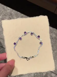Detailed view of a silver-toned bracelet with purple zircons on a textured cream card