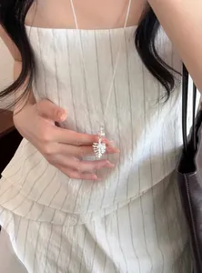 Gros plan d'un collier de perles argenté avec pendentif porté avec une robe à rayures.