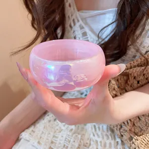 Vista detallada de un brazalete ancho transparente rosa iridiscente sostenido a mano.