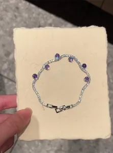 Detail view of a silver-toned bracelet featuring purple zircons on a textured pad