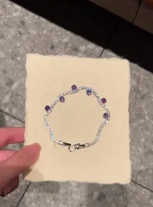 Detailed view of silver zircon wavy bracelet with purple accents held on cream card
