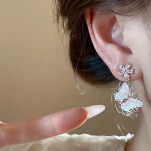 Close-up of zircon flower stud earring with a dangling butterfly pendant worn on ear.