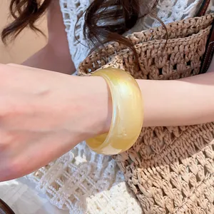 Vista detallada de un brazalete amarillo translúcido iridiscente ancho usado en la muñeca