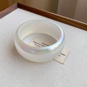 Detalle de un brazalete ancho transparente e iridiscente minimalista con un brillo vibrante aurora.
