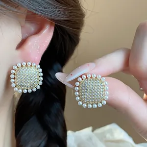 Close-up of elegant square stud earrings with pave zircon and pearl halo detail
