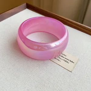 Primer plano detallado de un brazalete ancho de resina rosa translúcida e iridiscente
