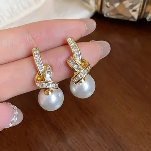 Close-up of elegant gold ribbon earrings with zircon crystals and round white pearls.