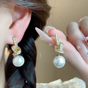 Close-up shot of elegant gold knot earrings with zircons and large dangling white pearls